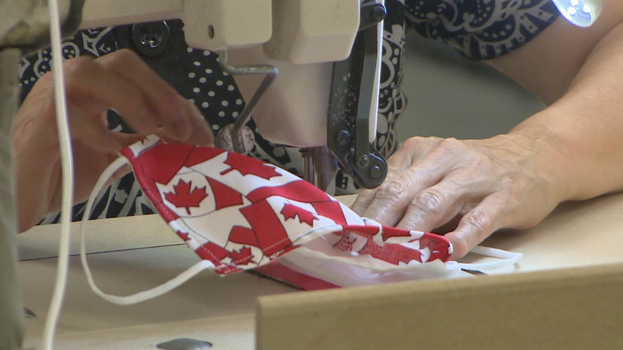 Un gros plan sur l'aiguille de la machine à coudre d'une femme qui effectue la finition d'un masque aux couleurs du drapeau canadien.