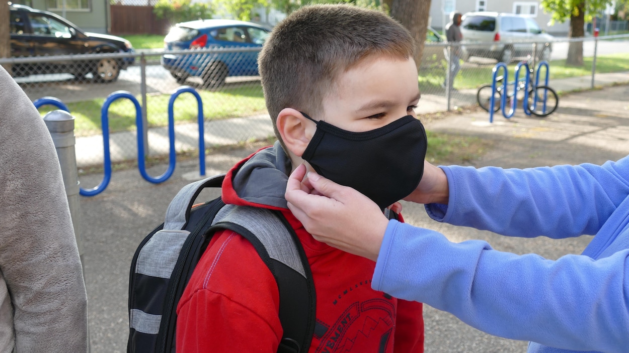 Une adulte met un masque sur le visage d'un écolier.