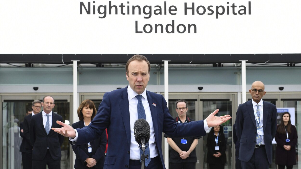 Matt Hancock parle dans un micro entouré de gens devant la façade de l'hôpital.