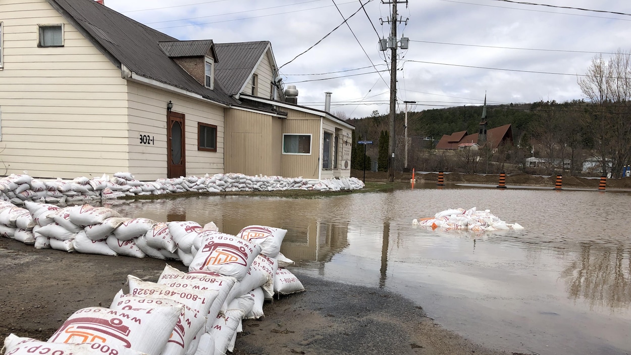 Des sacs de sable protègent une maison de l’eau qui déborde de la rivière.