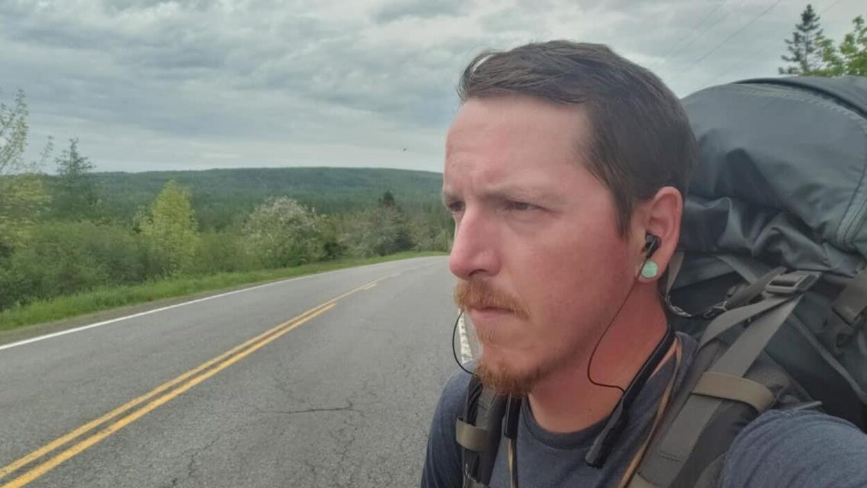 Un homme de profil avec des écouteurs et un sac à dos, en bord de route