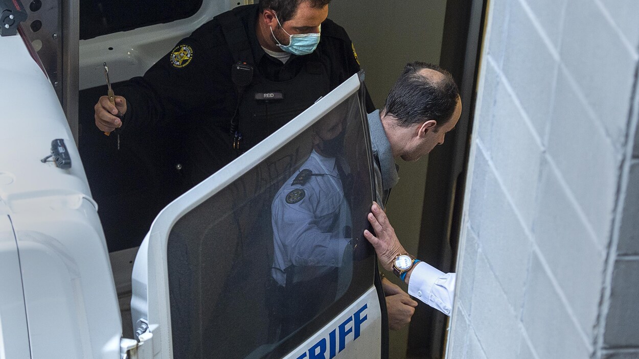 Menotté et escorté de policiers, Matthew Raymond descend d'un véhicule du shérif dont la porte s'ouvre directement sur une porte du palais de justice.