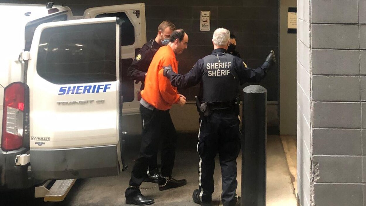 Matthew Raymond est accompagné à l'extérieur d'un fourgon de police par deux agents.