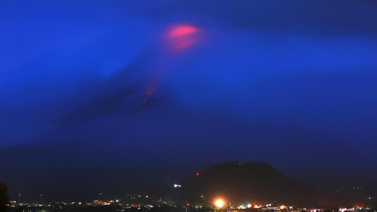 Un point rougeoyant contraste sur un ciel bleu nuit alors que le volcan Mayon, couvert par les nuages, entre en éruption. Un point rougeoyant contraste sur un ciel bleu nuit alors que le volcan Mayon, couvert par les nuages, entre en éruption.