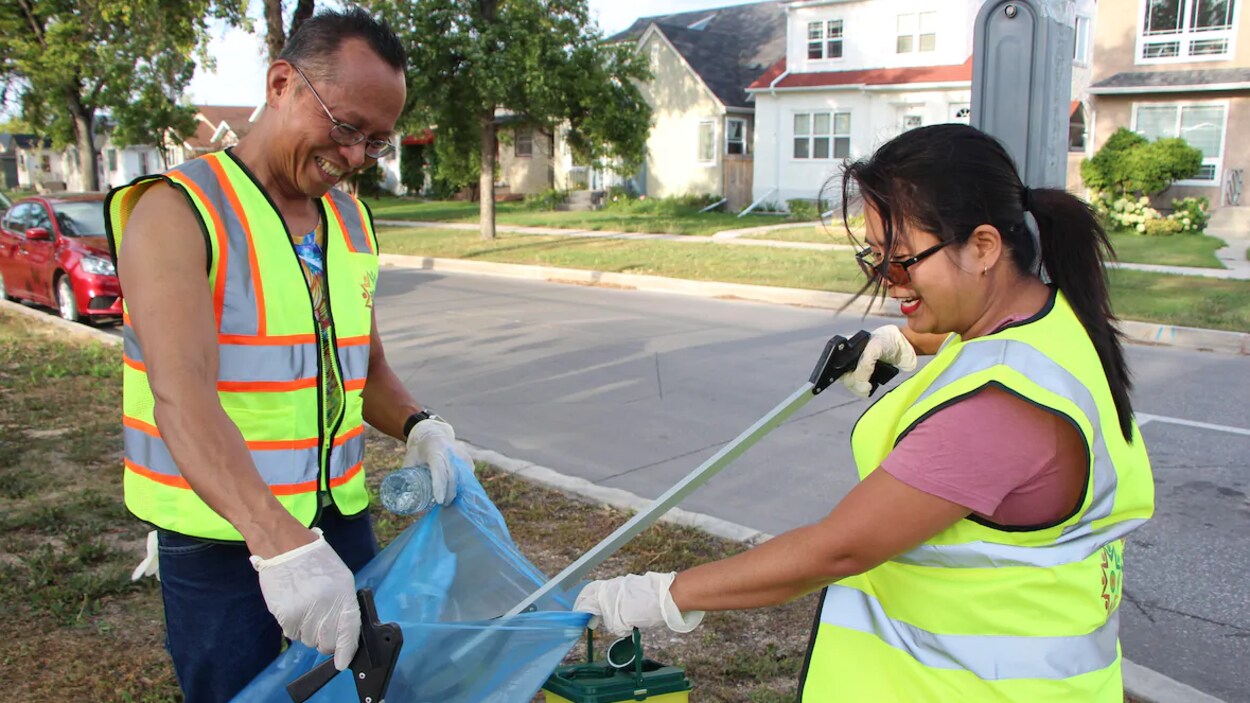 Un homme et une femme mettent des déchets dans un sac de plastique.