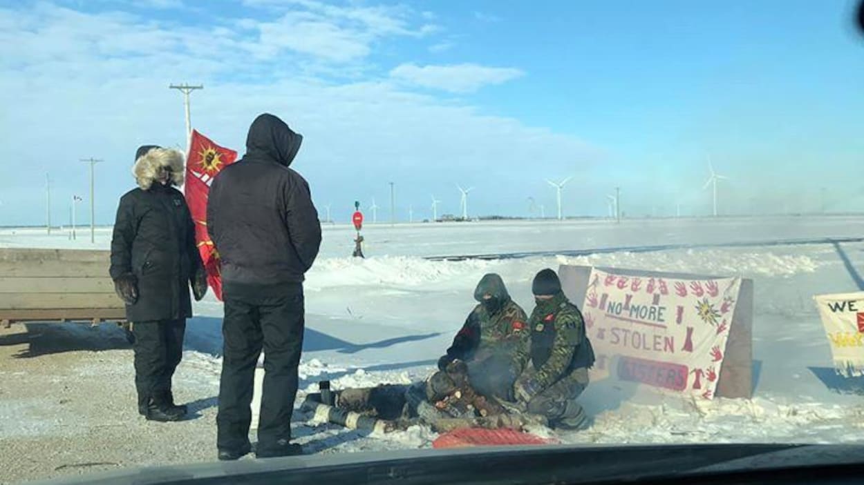 Deux manifestants debout et deux autres, assis, autour d'un feu de camp.