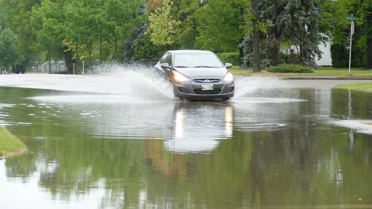 Une voiture traverse une rue inondée dans un quartier résidentiel.