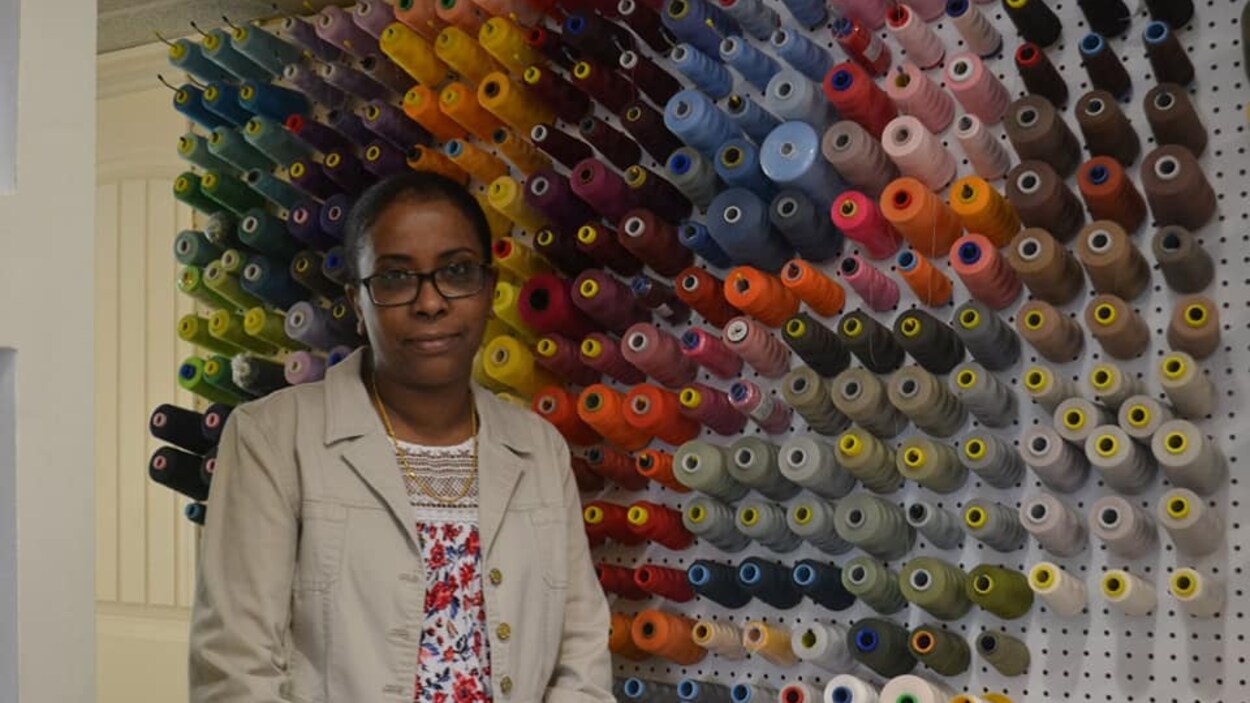 Mme Ahmed pose devant un mur couvert de bobines de fil.