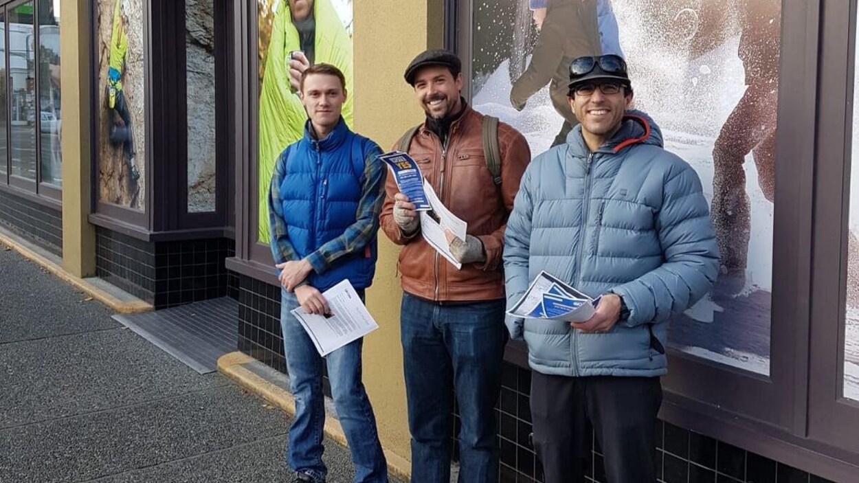 Trois hommes sourient devant un magasin MEC.