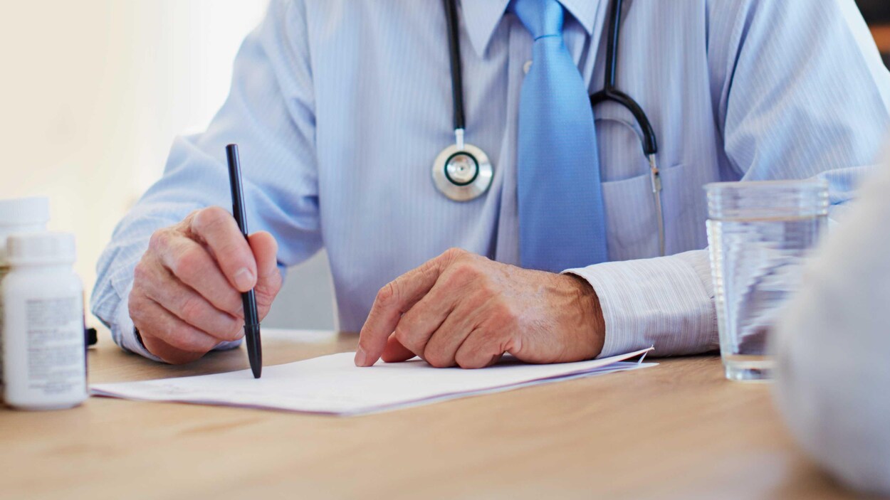 Les mains d'un médecin d'un certain âge en train de remplir un formulaire.