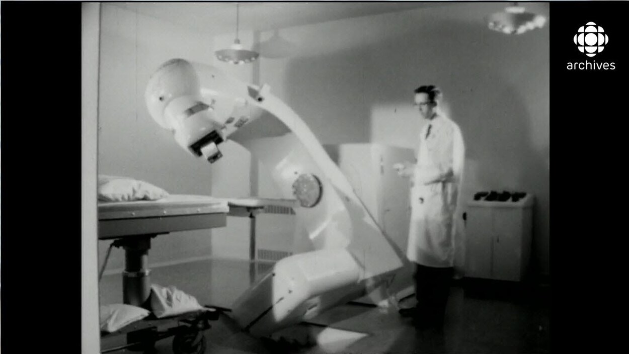 Homme en sarrau manipulant à l'aide d'une manette un gros appareil de médecine nucléaire qui entame une rotation Homme en sarrau manipulant à l'aide d'une manette un gros appareil de médecine nucléaire qui entame une rotation