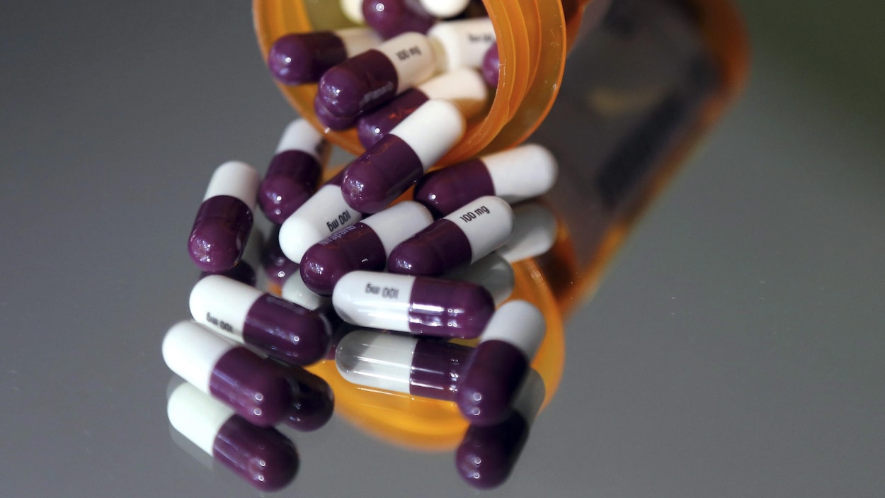 Des capsules blanches et mauves sortent d'un contenant de médicaments.