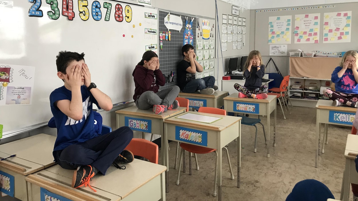 Des enfants sont assis sur leur pupitre, les mains sur les yeux, méditant.