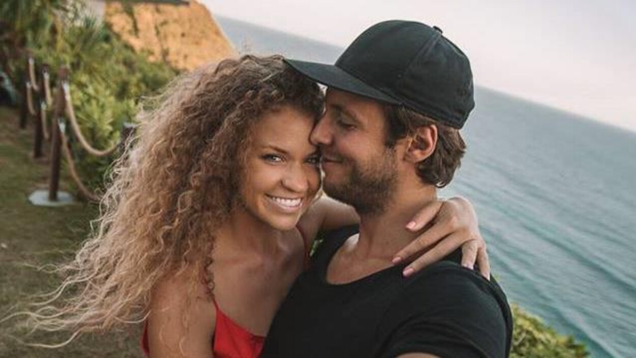 Une femme en robe rouge et un homme en t-shirt noir au bord de la mer.