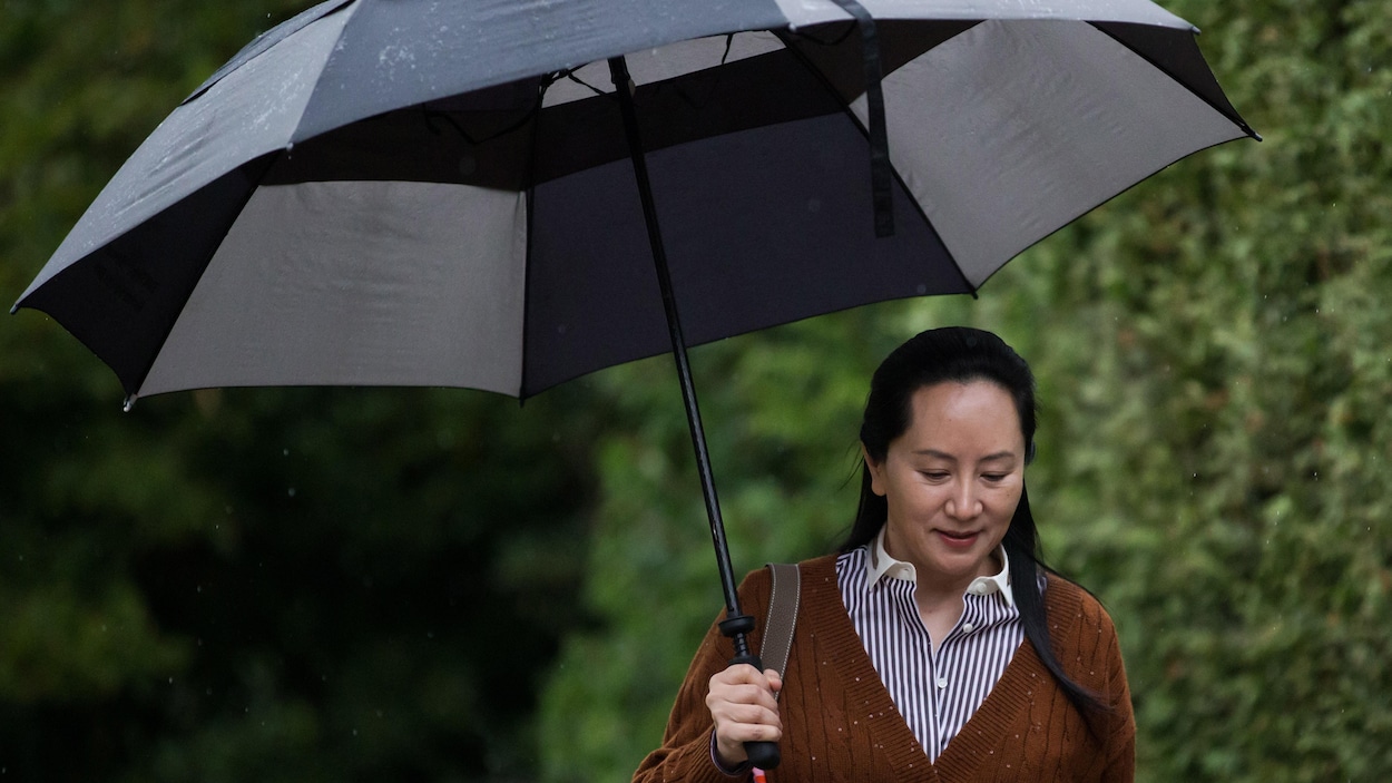 Plan moyen de Meng Wanzhou tenant un parapluie avec de hauts buissons verts en arrière-plan.