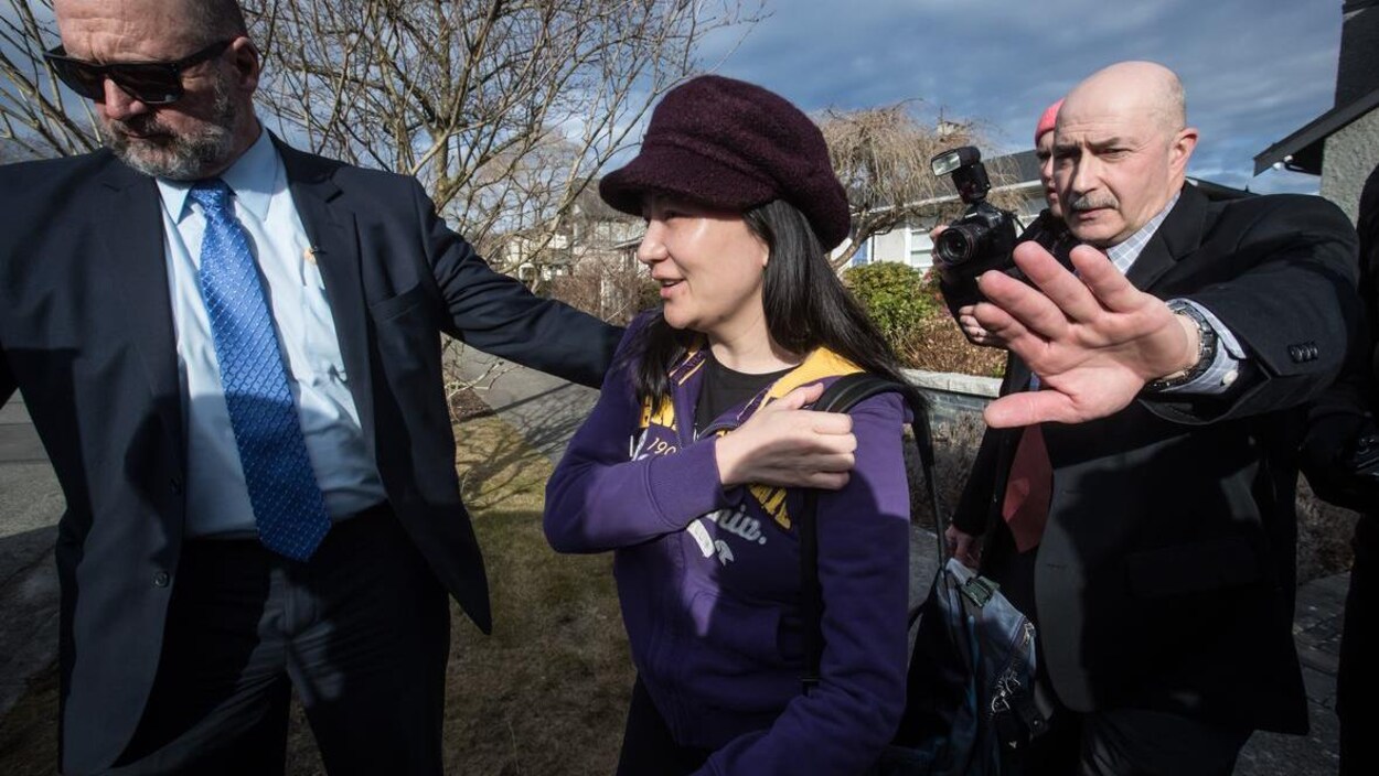 Meng Wanzhou sourit. Elle porte une casquette sombre.