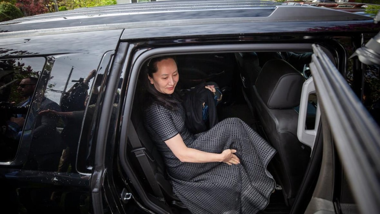 Une femme en robe entre dans une voiture noire.