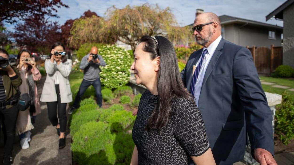Une femme marche à côté d'une garde de sécurité pendant que des gens la photographient.