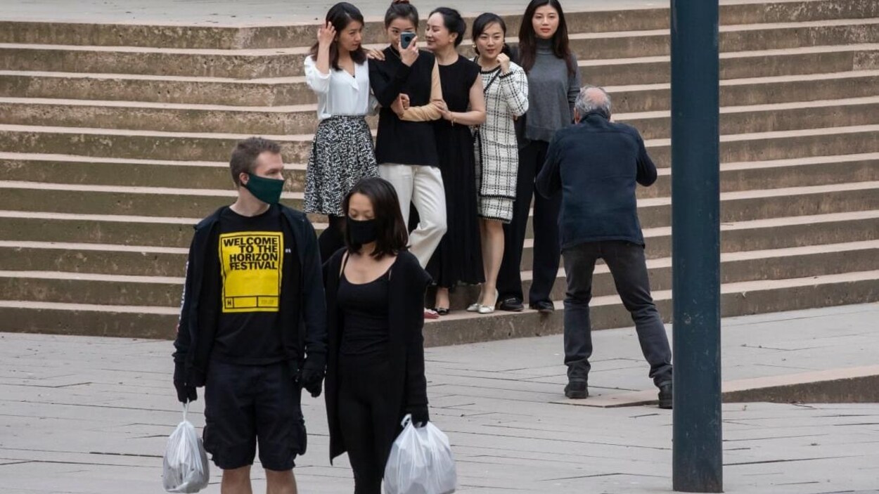 Un groupe de femmes, dont Meng Wanshou, se fait photographier sur des marches. Devant, un couple portant des masques marche.