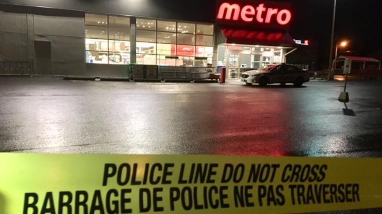 Un ruban jaune de barrage policier devant une voiture de police et une épicerie Metro.