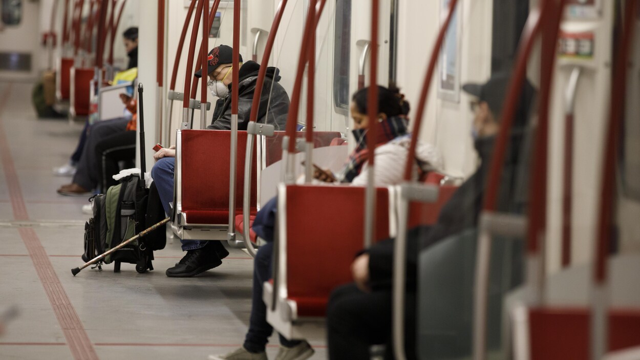 Plusieurs usagers sont assis à bonne distance les uns des autres dans une rame de métro. Certains portent des masques.