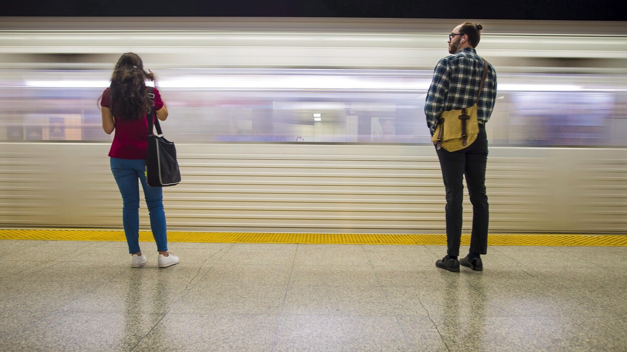Une femme et un homme sur le quai devant une rame de métro en marche