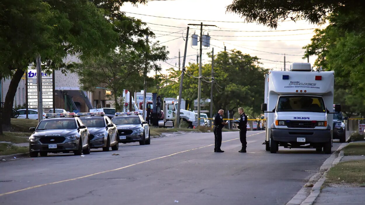 Deux agents discutent dans la rue près d’un véhicule de la police et d’autopatrouilles.