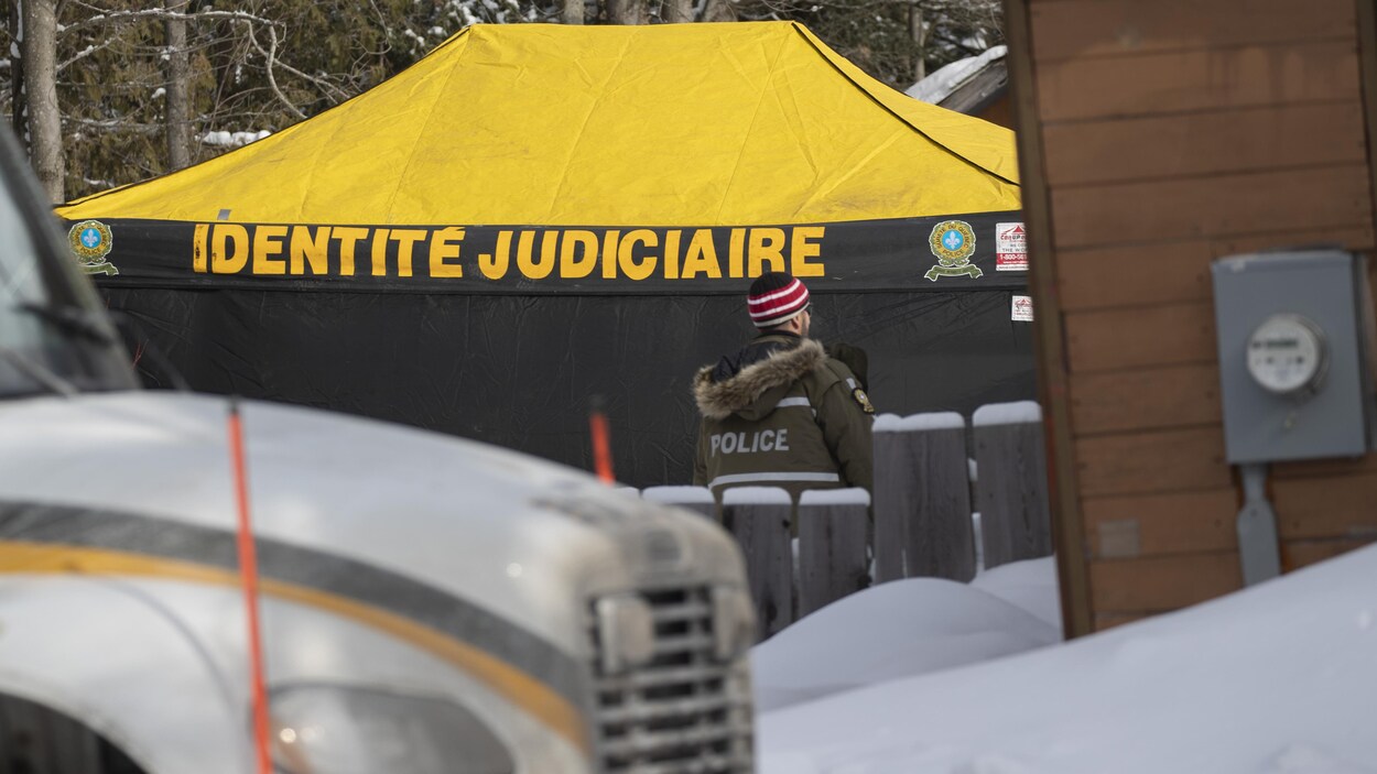 Un policier devant une tente de la SQ sur laquelle on peut lire «identité judiciaire».