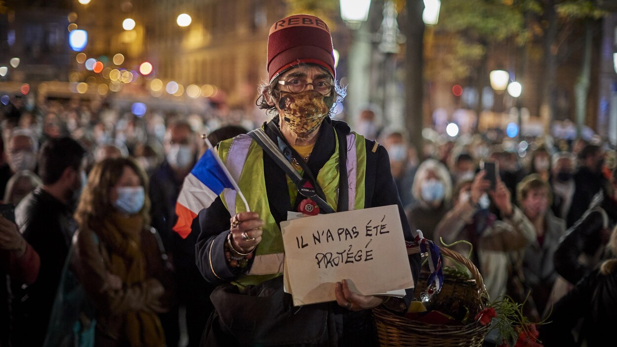 « Il n'a pas été protégé », peut-on lire sur une pancarte brandie par un manifestant masqué qui se tient debout dans une rue au milieu d'une foule.