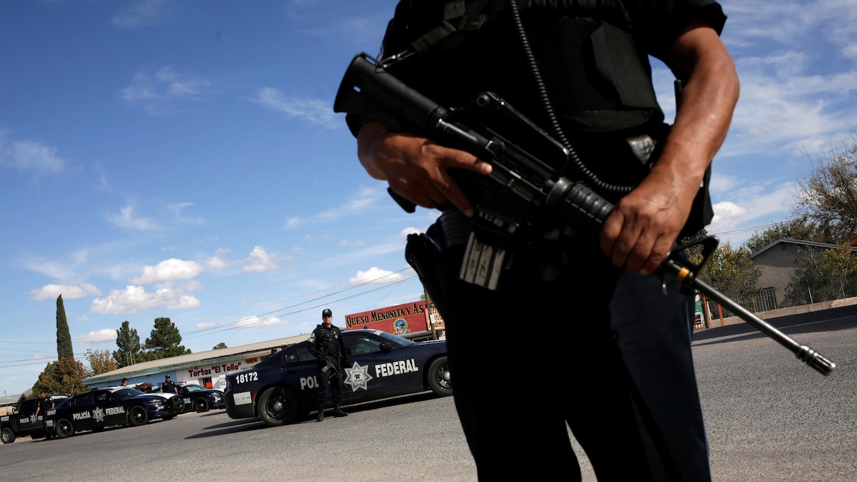 Un policier avec un fusil devant plusieurs voitures de police.