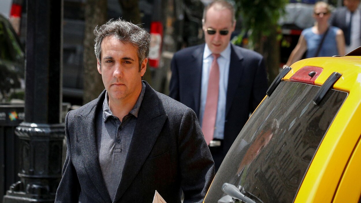 Un homme portant un complet traverse une rue de New York derrière un taxi jaune.