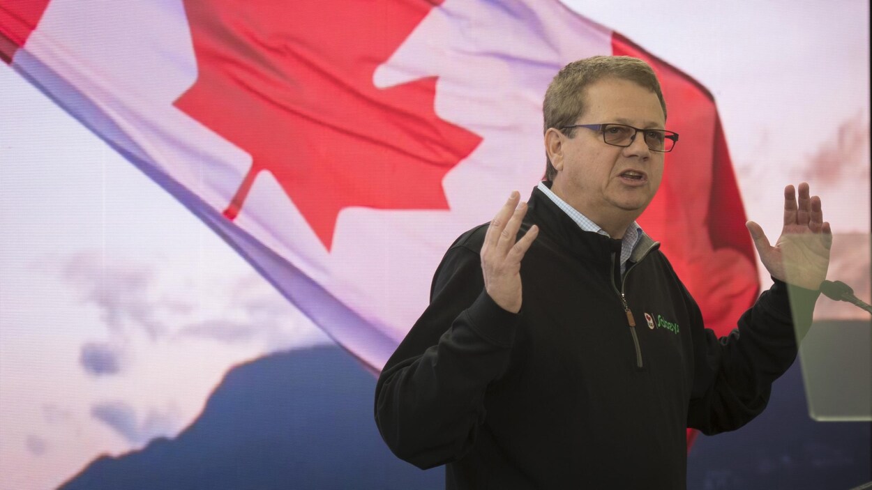 Michael Medline prononce une allocution et un grand drapeau du Canada flotte derrière.