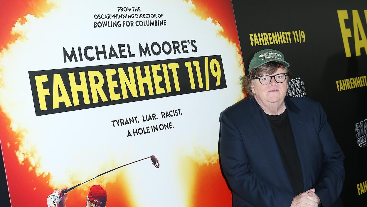 Michael Moore se tient devant une affiche de son film «Fahrenheit 11/9» en se tenant les mains.