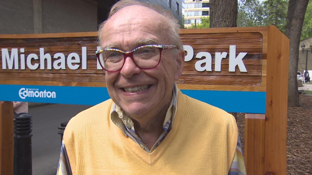 Plan serré de Michael Phair devant l'écriteau portant le nom de l'école rebaptisée en son honneur
