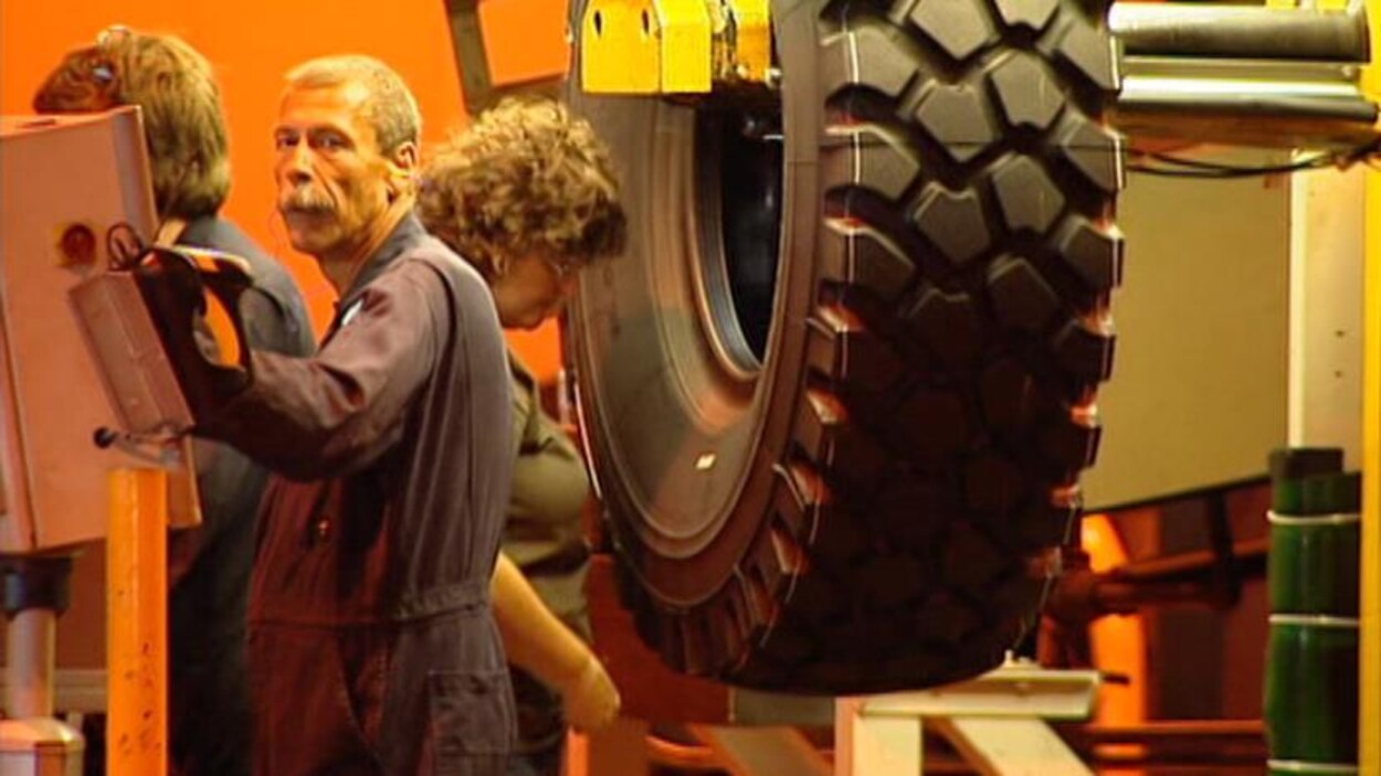 Trois travailleurs inspectent un pneu dans une usine.