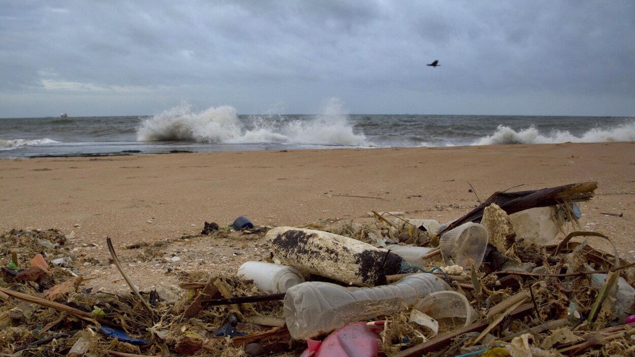 Des détritus en plastique sur une plage où la mer est agitée.