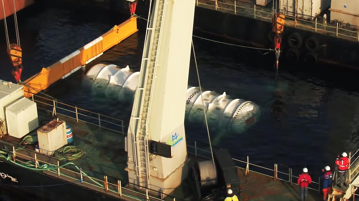 Une capture d'écran d'une vidéo montrant la capsule de Microsoft, attachée à une grue flottante, en train de descendre vers les profondeurs marines.