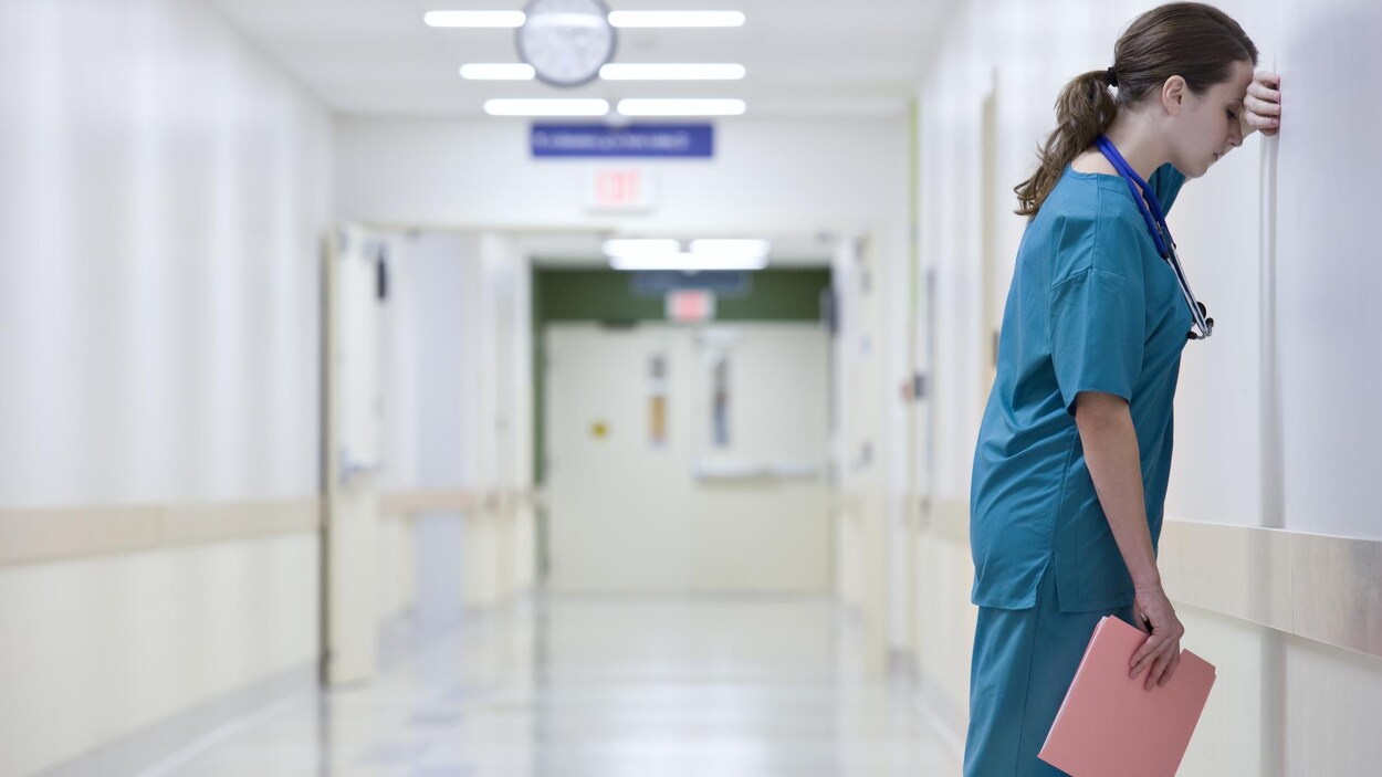 Une professionnelle de la santé est appuyée contre un mur dans un couloir d'hôpital. Une professionnelle de la santé est appuyée contre un mur dans un couloir d'hôpital.