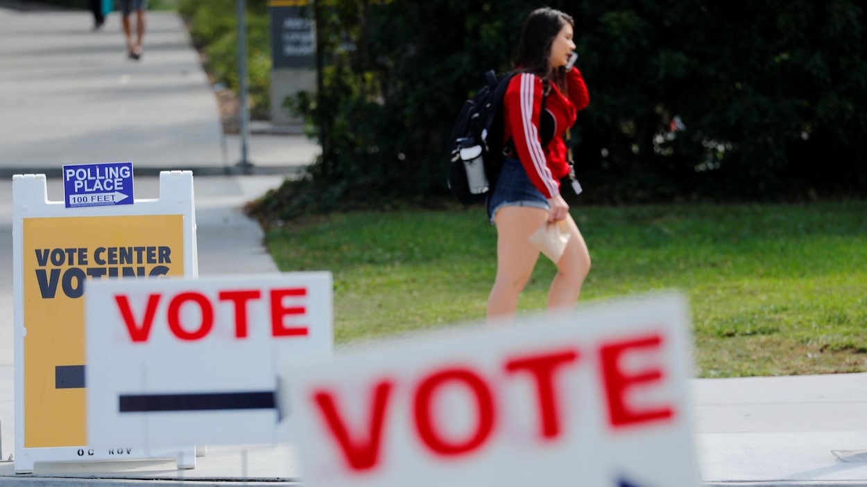 Une jeune femme parle au téléphone alors qu'elle marche près de pancartes indiquant où aller voter.