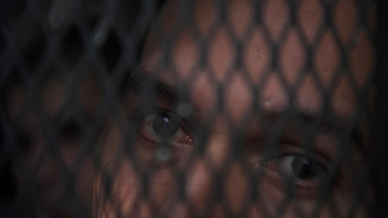 Un membre de la Mara Salvatrucha, alias MS-13, dont les yeux sont visibles derrière une grille dans un centre de détention au Salvador.