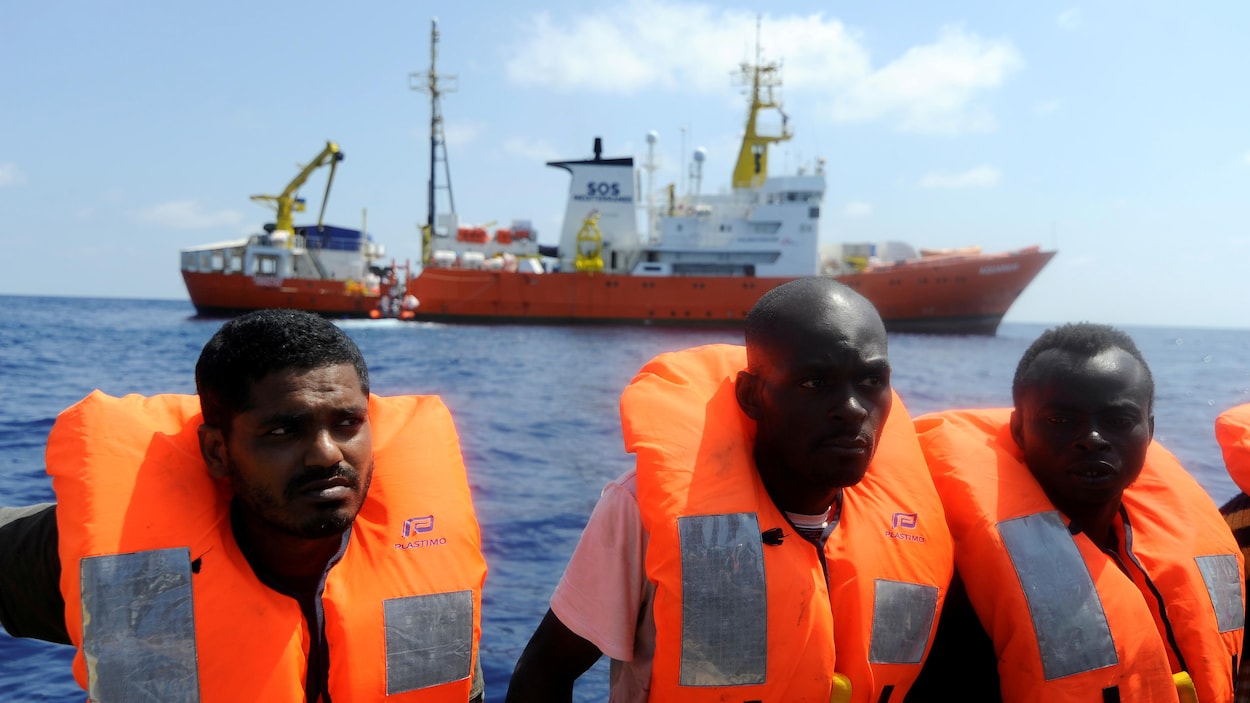 Des hommes assis dans un bateau munis de vestes de sauvetage.