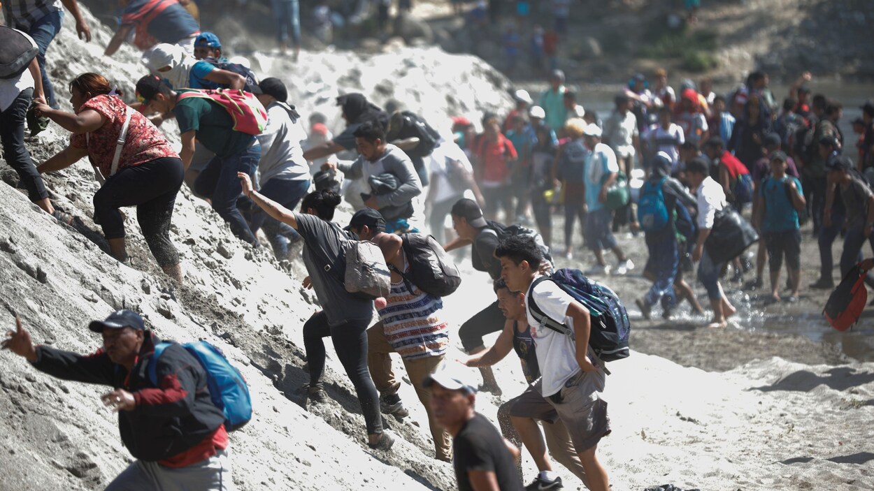 Une foule de gens tentent de grimper un talus de sable et de pierre.
