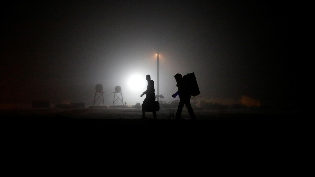 Deux hommes marchent sur des rails de chemin de fer en pleine nuit.