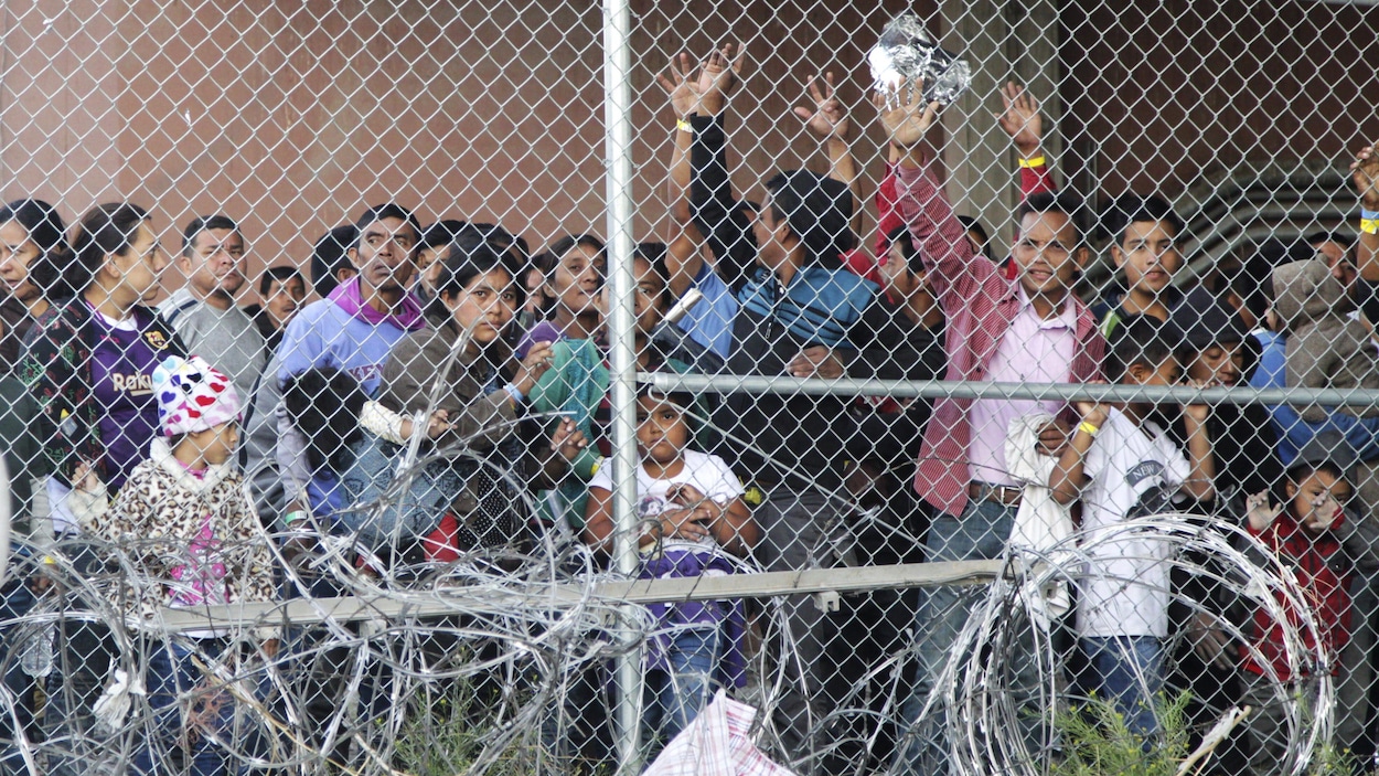 Des migrants font un signe de salutation avec la main derrière une grille.