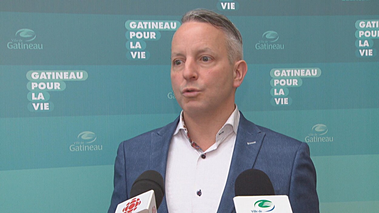 Mike Duggan s'adresse aux médias devant une bannière comportant le logo de la Ville de Gatineau.