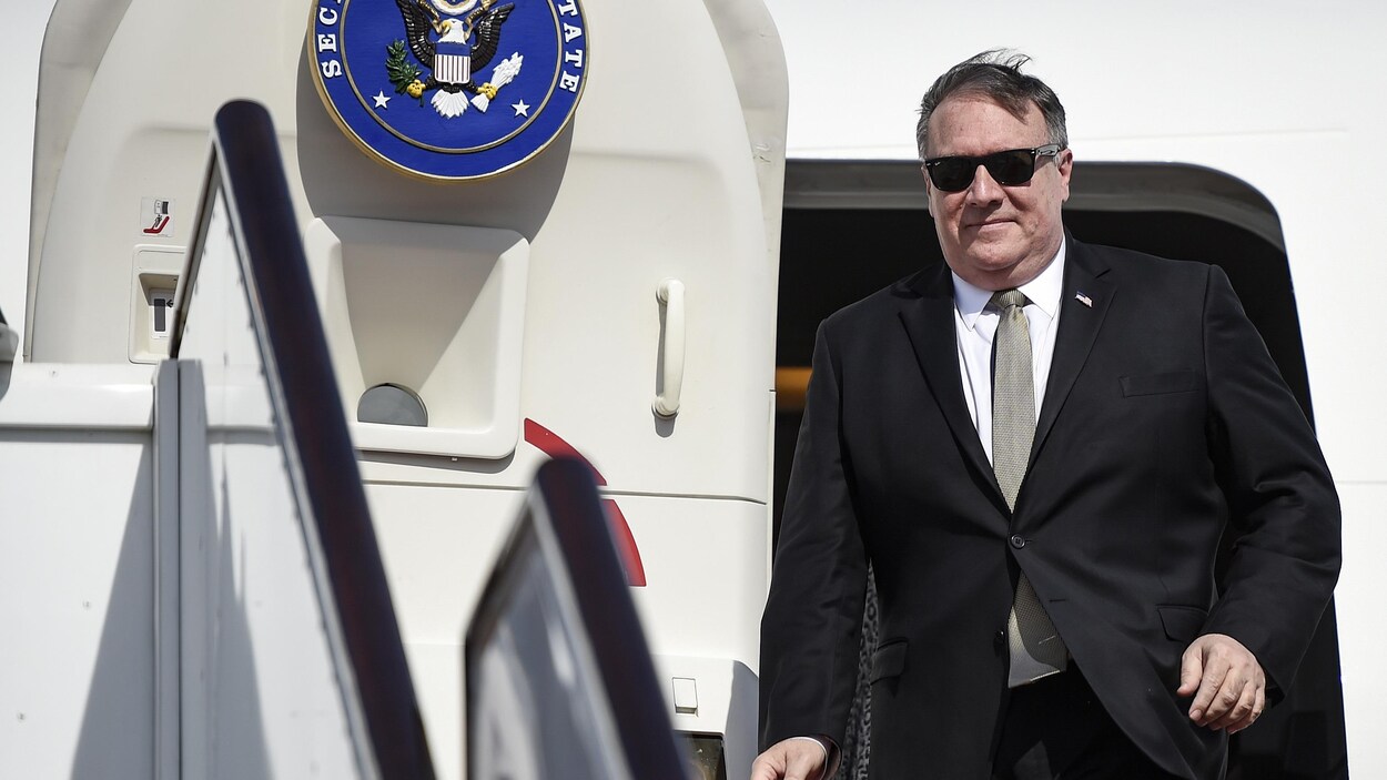 Mike Pompeo, portant un complet avec une cravate et des lunettes de soleil, sort d'un avion.