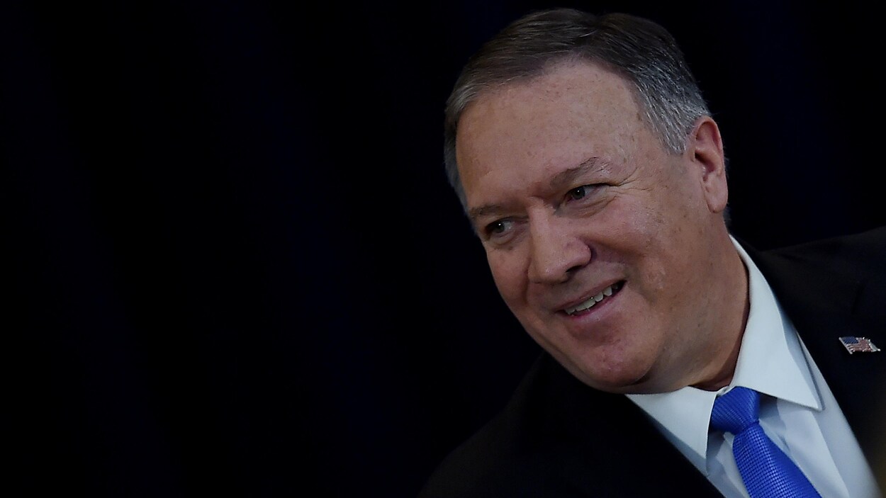 Mike Pompeo sourit devant une toile noire.