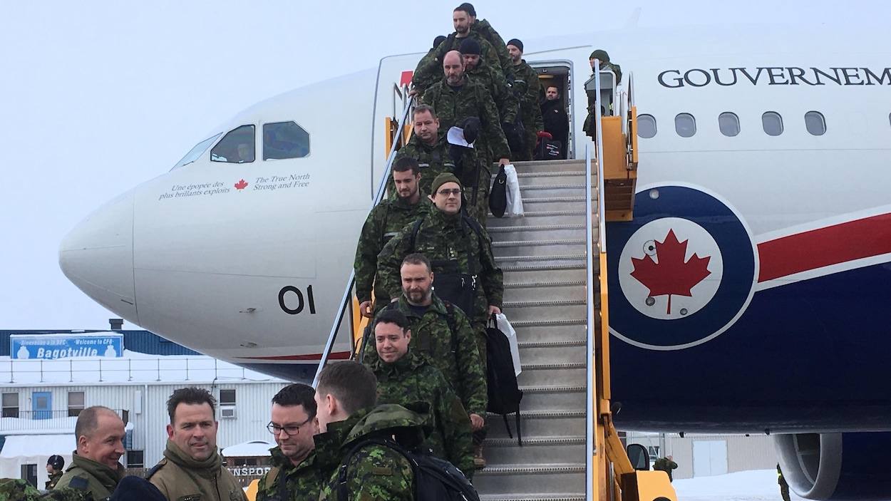 Plusieurs hommes en uniforme militaire descendent l'escalier d'un avion posé sur le tarmac à Bagotville.