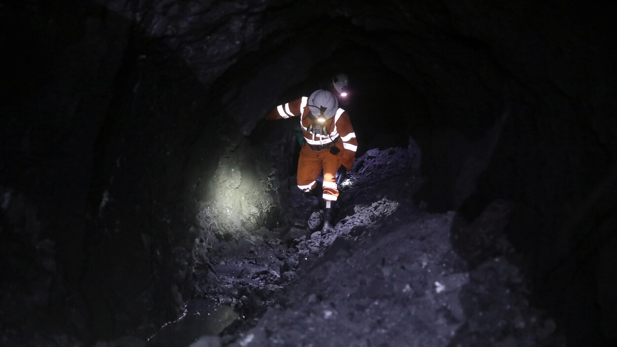 Un mineur vêtu d'une combinaison et d'un casque de protection marche à l'intérieur d'une mine.