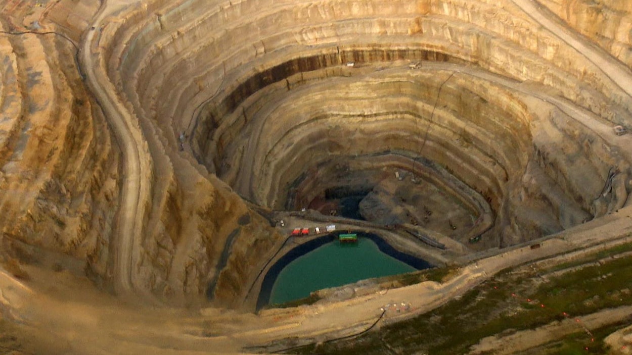 Vue aérienne d'un puits de mine à ciel ouvert. On aperçoit un bassin d'eau et des véhicules miniers.